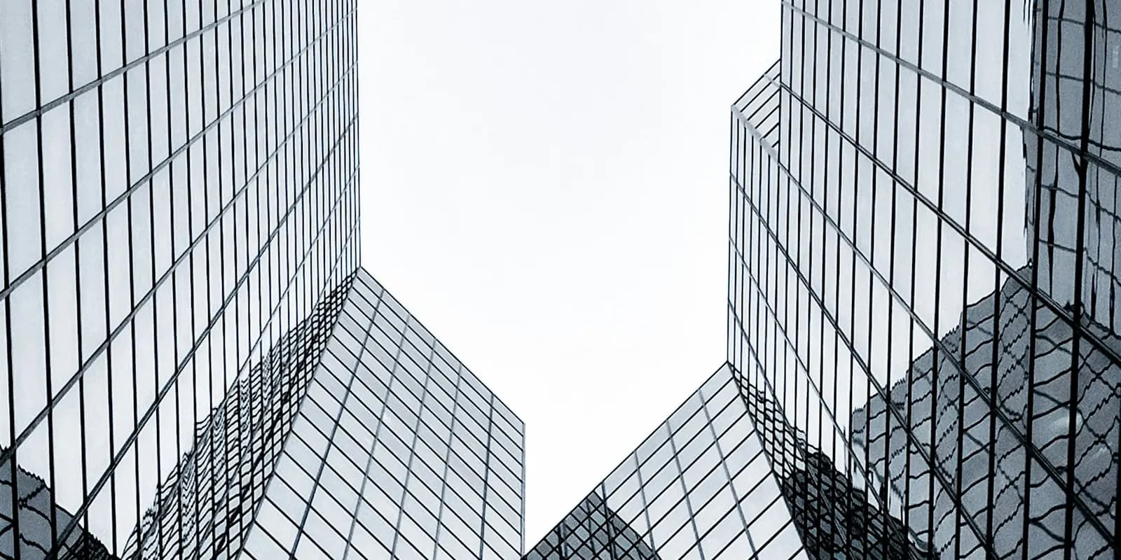 Glass office towers of different shapes photographed from below against a bright sky.