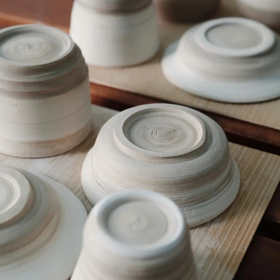 Wheel-thrown white bowls stacked upside down on a workshop bench, still unglazed.