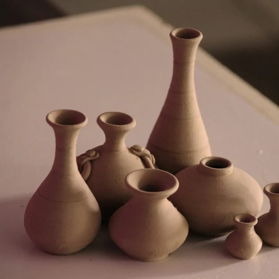 Eight unglazed terracotta vessels of varying height grouped on a dusty pink ground.