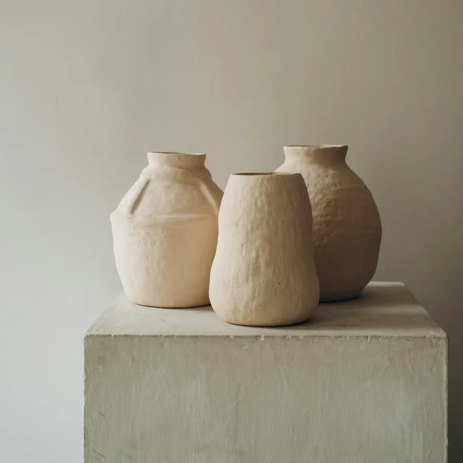 Three pale hand-pinched vases with visible finger marks, sitting on a concrete plinth.